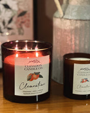 Load image into Gallery viewer, Two Clevedon Candle Co Clementine candles on a wooden surface with a decorative vase in the background.