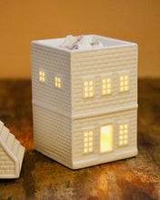 Load image into Gallery viewer, White ceramic building-shaped lamp with lit windows on a wooden surface